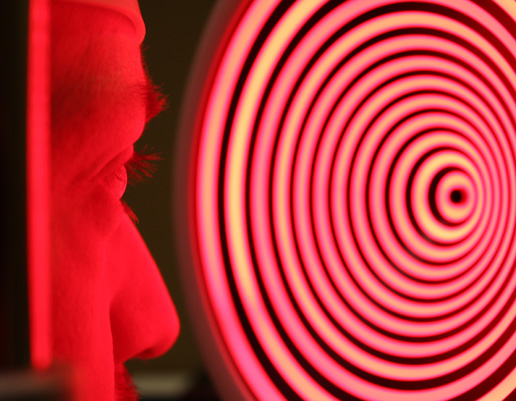 Nahaufnahme eines Gesichts im Profil vor einer rot leuchtenden Zielscheibe mit konzentrischen Ringen.